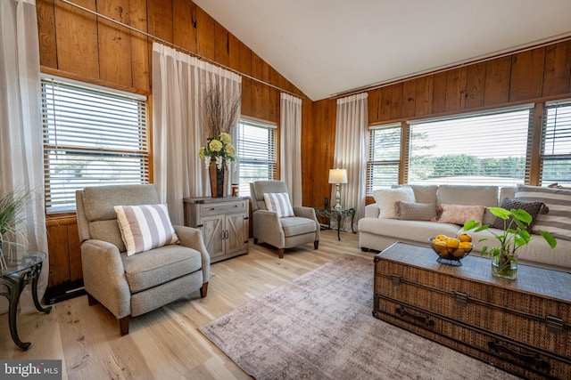 sitting room featuring light wood-type flooring, wood walls, lofted ceiling, and plenty of natural light