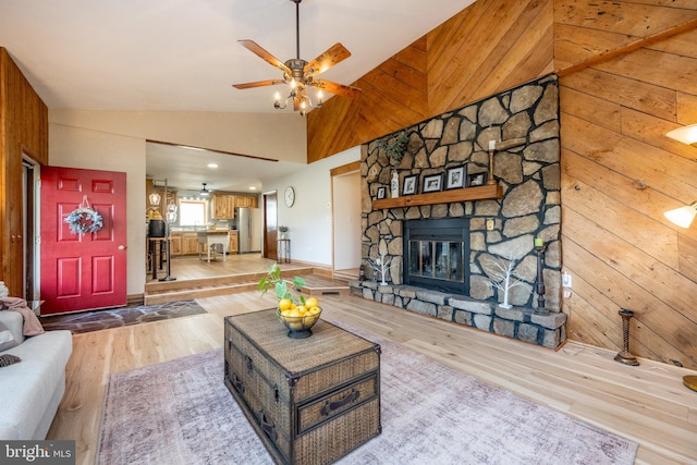 living room with wood walls, a stone fireplace, light hardwood / wood-style flooring, high vaulted ceiling, and ceiling fan