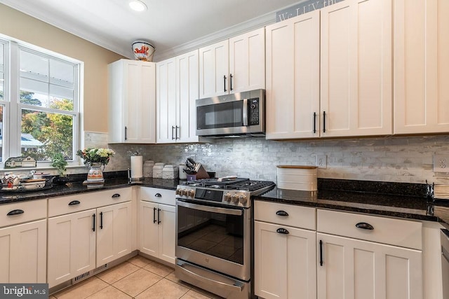 kitchen with light tile patterned floors, appliances with stainless steel finishes, dark stone counters, and white cabinets