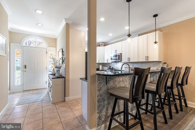 kitchen featuring kitchen peninsula, white cabinets, tasteful backsplash, a breakfast bar area, and crown molding