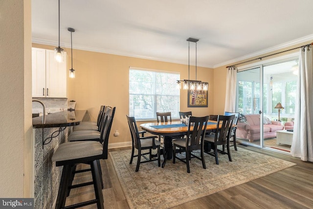 dining room with dark wood-type flooring, ornamental molding, and an inviting chandelier