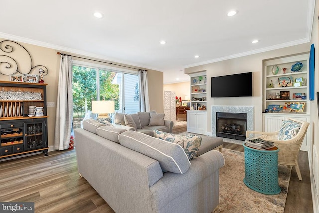 living room with a high end fireplace, crown molding, built in shelves, and wood-type flooring