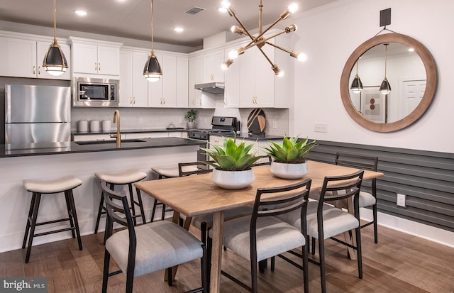 dining area featuring sink, dark wood-type flooring, crown molding, and an inviting chandelier