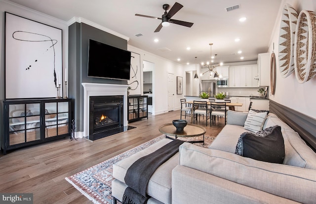 living room with crown molding, ceiling fan with notable chandelier, and light wood-type flooring