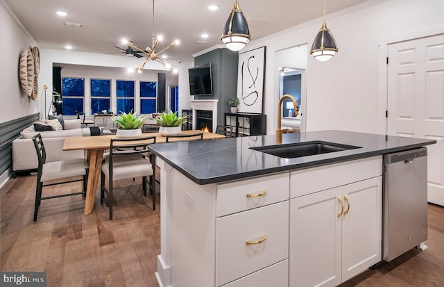 kitchen with white cabinets, an island with sink, hardwood / wood-style flooring, stainless steel dishwasher, and sink