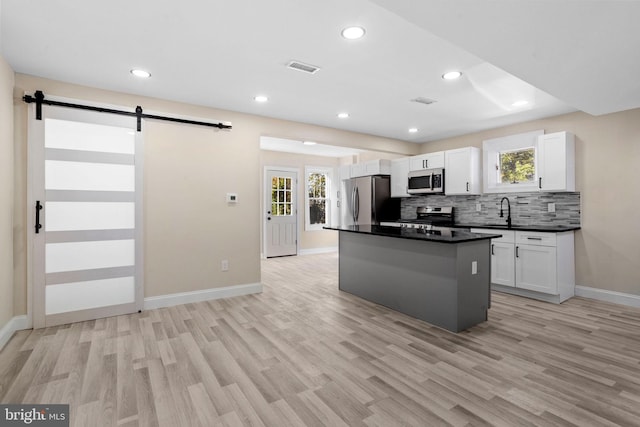 kitchen with a kitchen island, stainless steel appliances, a barn door, light wood-type flooring, and white cabinetry