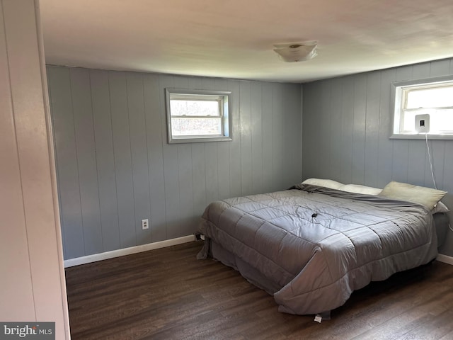 bedroom featuring multiple windows, dark hardwood / wood-style flooring, and wood walls