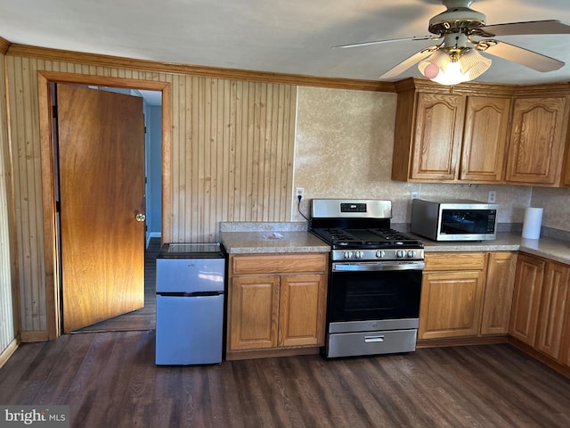 kitchen featuring dark hardwood / wood-style flooring, ceiling fan, stainless steel appliances, wooden walls, and ornamental molding