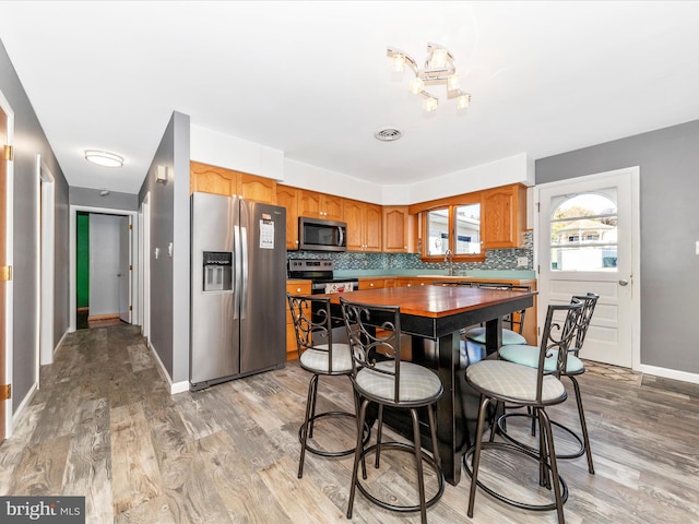 kitchen with light hardwood / wood-style floors, decorative backsplash, stainless steel appliances, and sink