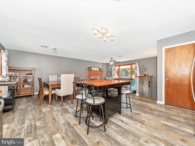 dining area featuring light hardwood / wood-style flooring, a brick fireplace, and ceiling fan