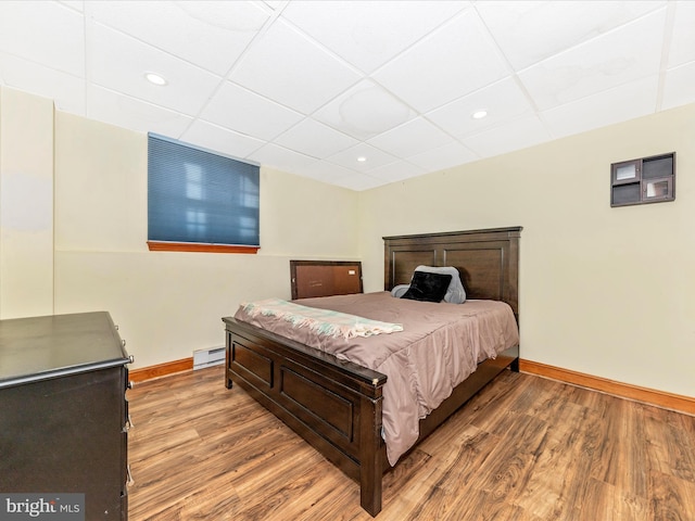 bedroom with a baseboard radiator, hardwood / wood-style floors, and a drop ceiling