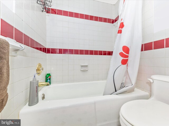 bathroom with tile walls, shower / bath combination with curtain, and toilet