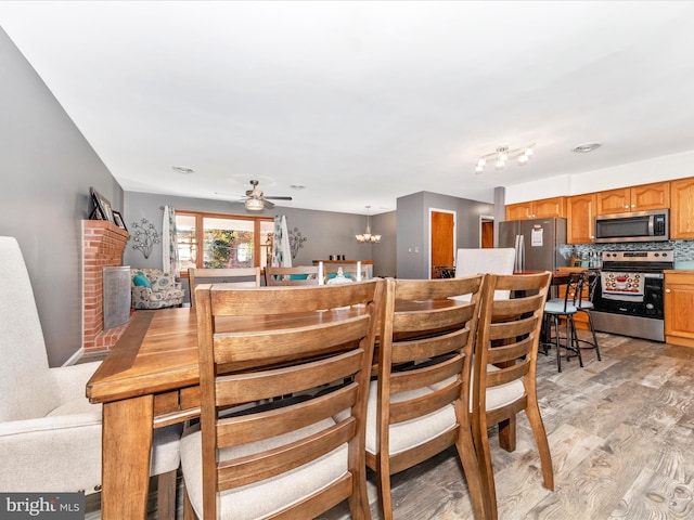 dining room featuring a brick fireplace, ceiling fan with notable chandelier, and light wood-type flooring