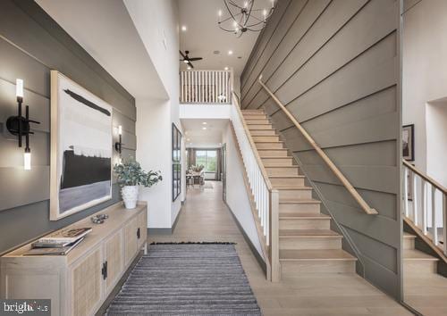 staircase featuring a towering ceiling, ceiling fan with notable chandelier, and hardwood / wood-style floors