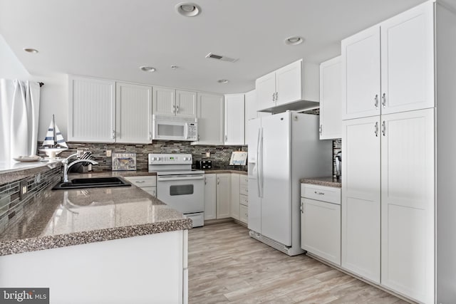 kitchen with white cabinets, dark stone counters, light hardwood / wood-style floors, sink, and white appliances