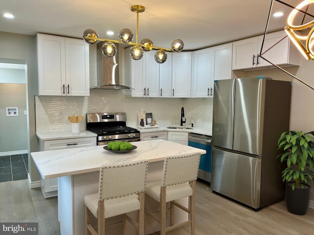 kitchen featuring wall chimney range hood, stainless steel appliances, pendant lighting, light wood-type flooring, and white cabinets