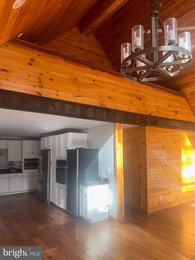 kitchen featuring oven, white cabinets, hardwood / wood-style floors, stainless steel refrigerator, and lofted ceiling with beams