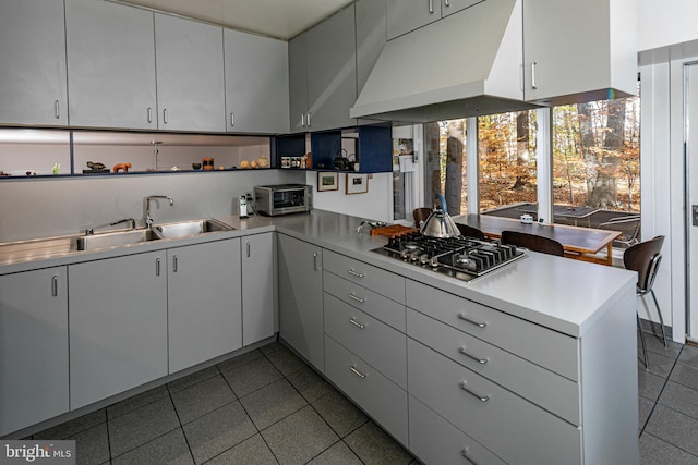 kitchen with kitchen peninsula, stainless steel gas stovetop, white cabinets, and sink