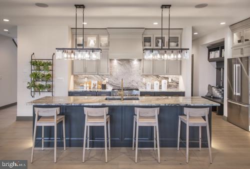 kitchen with a kitchen island with sink, decorative light fixtures, a kitchen breakfast bar, and stainless steel fridge