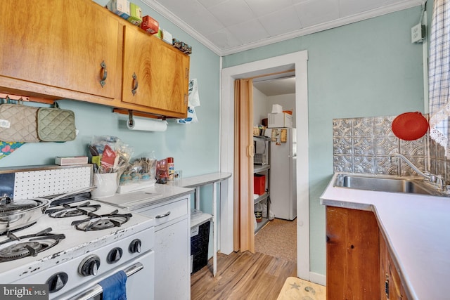 kitchen featuring a sink, white appliances, crown molding, light wood-style flooring, and light countertops