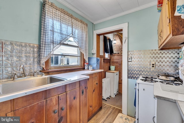 kitchen with white gas range, radiator, ornamental molding, sink, and light wood-type flooring