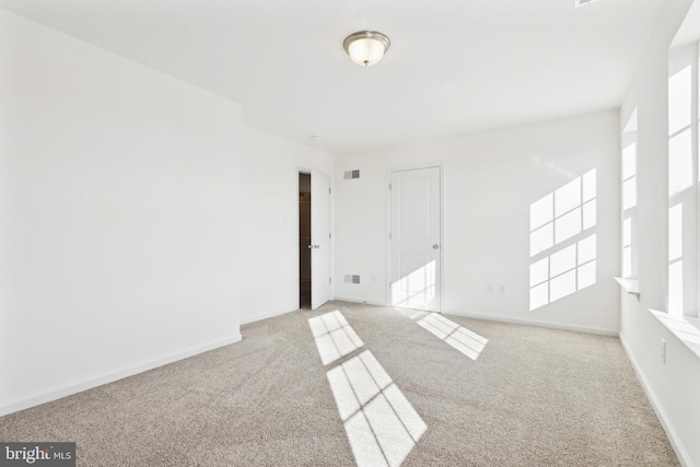 spare room with light carpet, visible vents, and baseboards