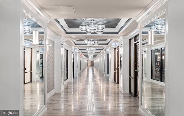 hallway featuring a raised ceiling, crown molding, wood-type flooring, and an inviting chandelier