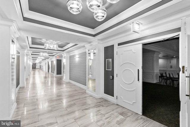 hallway with ornate columns, ornamental molding, a notable chandelier, and a tray ceiling