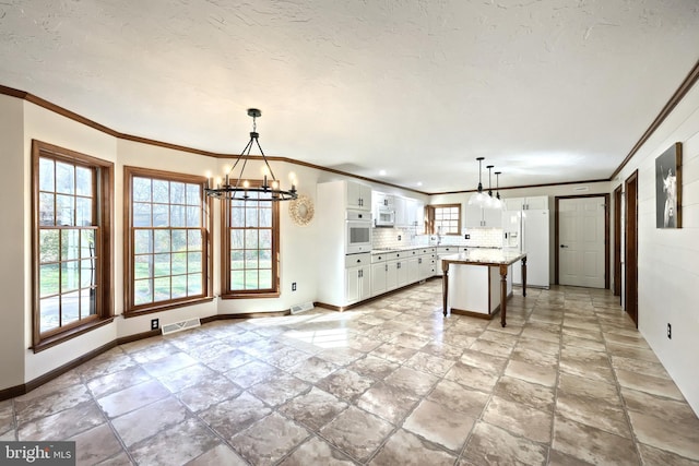 kitchen with white appliances, hanging light fixtures, a kitchen island, and white cabinets