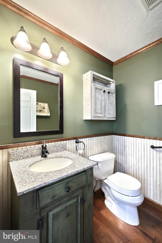 bathroom with a textured ceiling, wood-type flooring, toilet, ornamental molding, and vanity