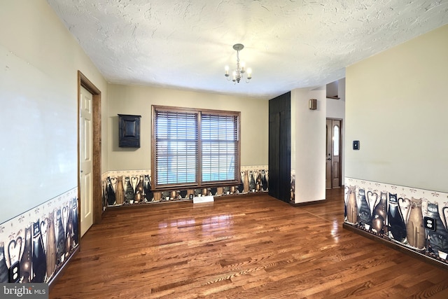 unfurnished room with a chandelier, a textured ceiling, and dark hardwood / wood-style flooring