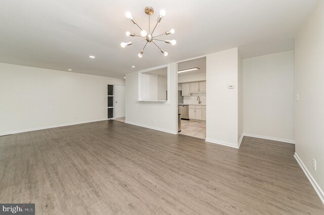 unfurnished living room featuring sink, a notable chandelier, and light hardwood / wood-style flooring