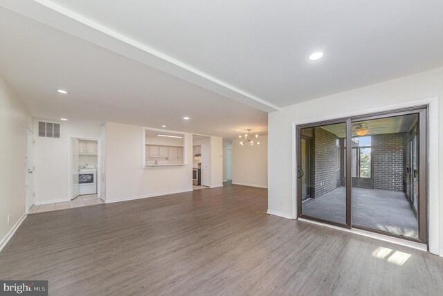 unfurnished living room with hardwood / wood-style floors, ceiling fan with notable chandelier, and washer / clothes dryer