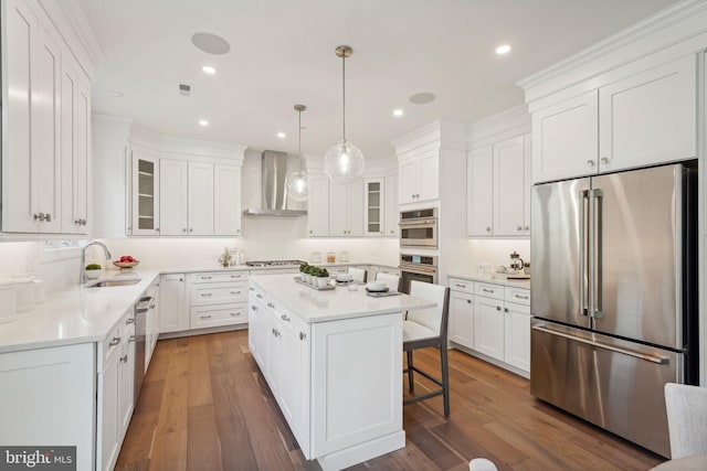 kitchen featuring dark wood-type flooring, white cabinets, wall chimney exhaust hood, appliances with stainless steel finishes, and a kitchen island