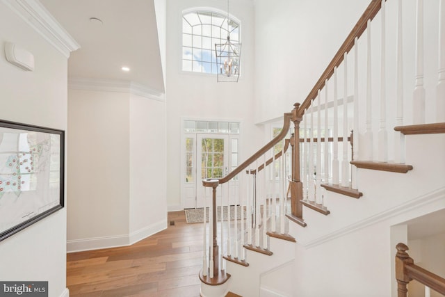 entrance foyer featuring an inviting chandelier, a towering ceiling, ornamental molding, and light wood-type flooring