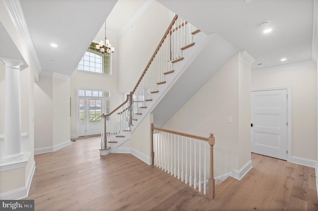 foyer entrance featuring a chandelier, light hardwood / wood-style floors, decorative columns, and crown molding