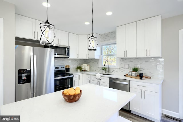 kitchen featuring white cabinetry, decorative backsplash, stainless steel appliances, and hanging light fixtures