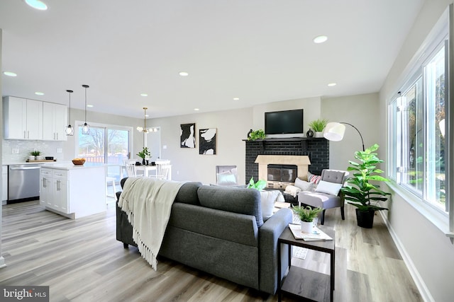 living room with a brick fireplace, light hardwood / wood-style floors, and a chandelier