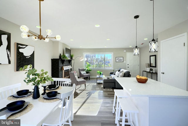 kitchen with pendant lighting, hardwood / wood-style floors, a kitchen breakfast bar, a brick fireplace, and a chandelier