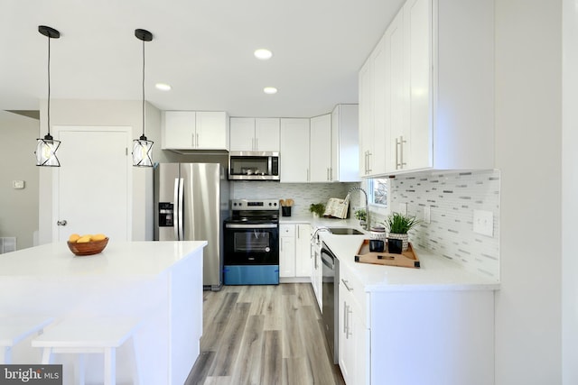 kitchen featuring white cabinetry, sink, appliances with stainless steel finishes, hanging light fixtures, and light wood-type flooring