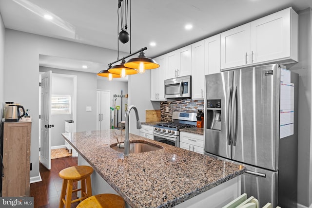 kitchen featuring appliances with stainless steel finishes, white cabinetry, dark stone countertops, dark wood-type flooring, and sink