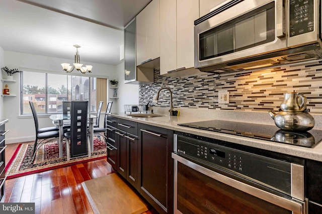 kitchen featuring appliances with stainless steel finishes, backsplash, dark wood-type flooring, a chandelier, and hanging light fixtures