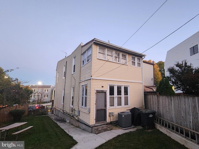 rear view of house featuring central AC and a lawn