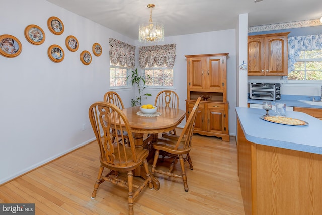 dining room featuring baseboards, a toaster, light wood-style flooring, and a notable chandelier