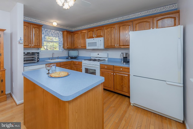 kitchen featuring white appliances, brown cabinetry, a kitchen island, light countertops, and a sink