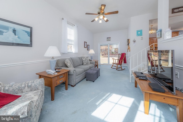 living room featuring light colored carpet, ceiling fan, and stairway