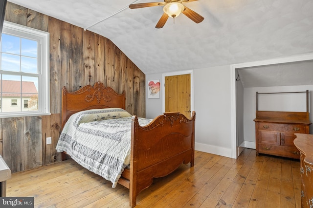 bedroom with wooden walls, light hardwood / wood-style floors, and lofted ceiling