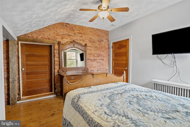 bedroom featuring ceiling fan, brick wall, vaulted ceiling, and hardwood / wood-style flooring