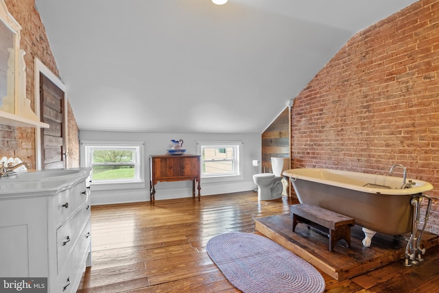 interior space with light hardwood / wood-style flooring, a wealth of natural light, lofted ceiling, and brick wall