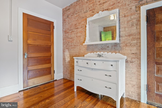 interior space featuring wood-type flooring, vanity, and brick wall